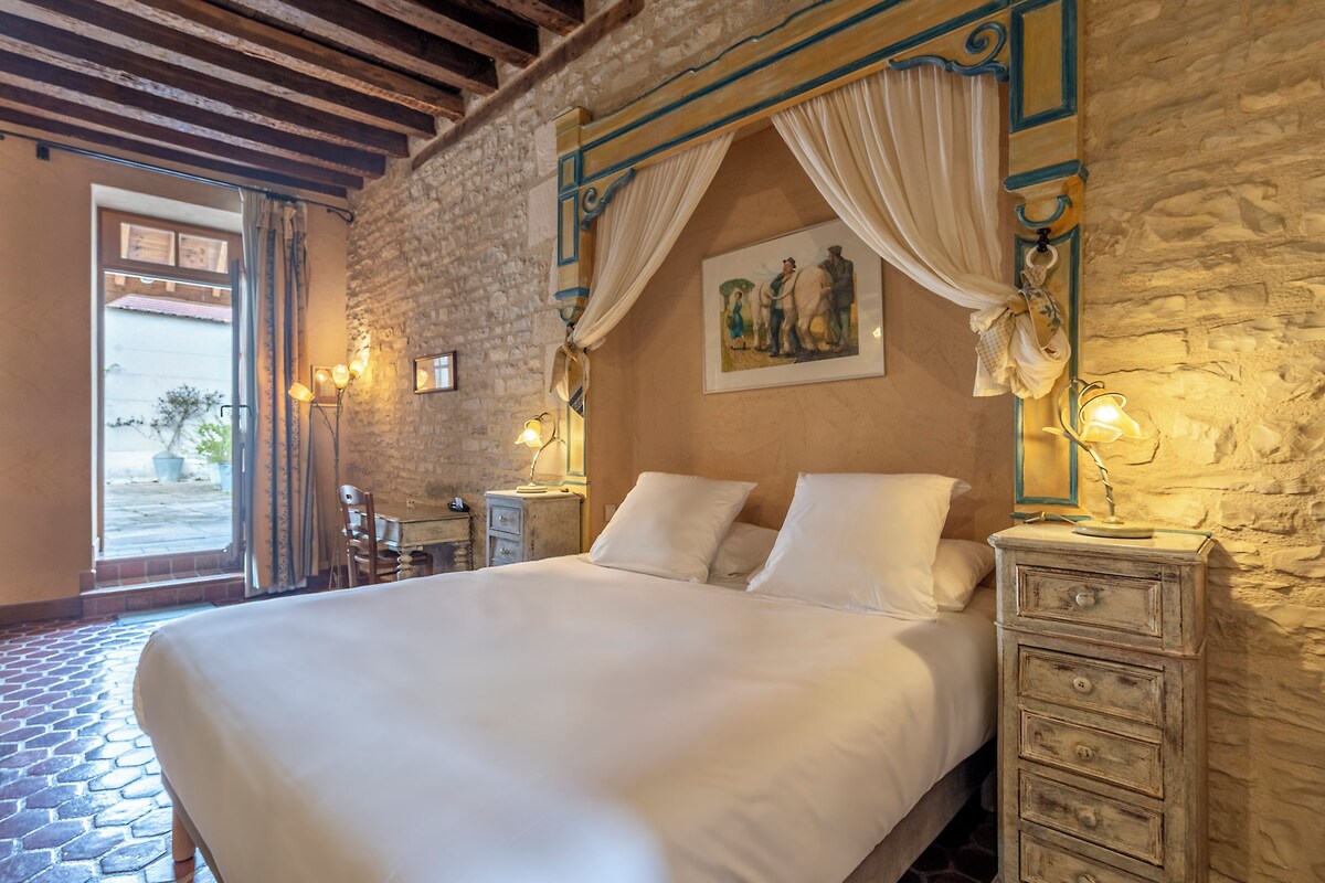 A bedroom with a large bed, stone walls, and a view through an open door.