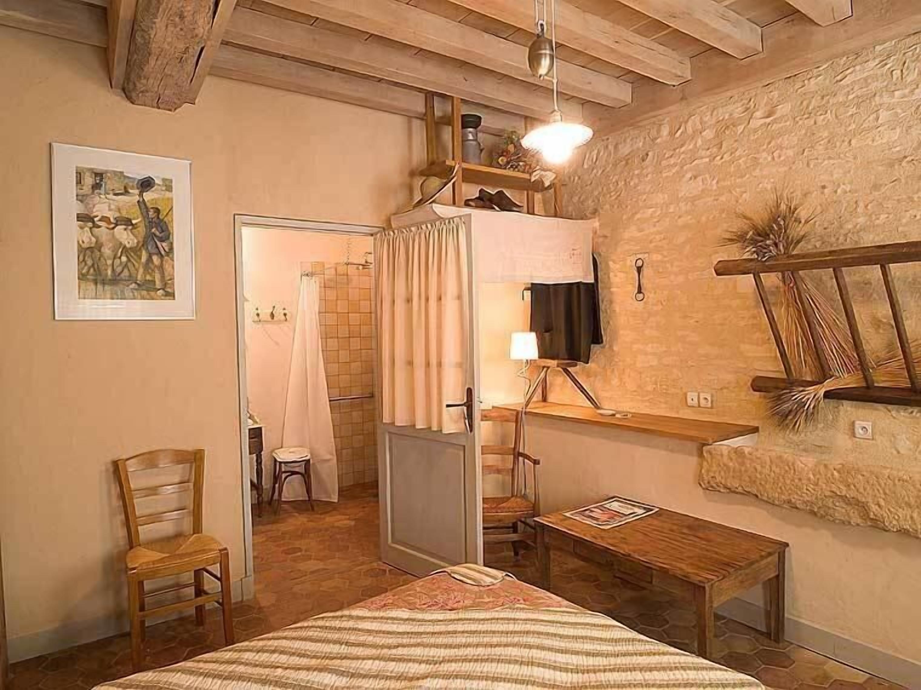 A rustic room with a bed, a chair, a desk, a lamp, and a shower area.