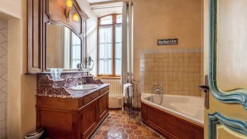 Un baño con un espejo grande, dos lavamanos, una bañera y un ventanal con cortinas.