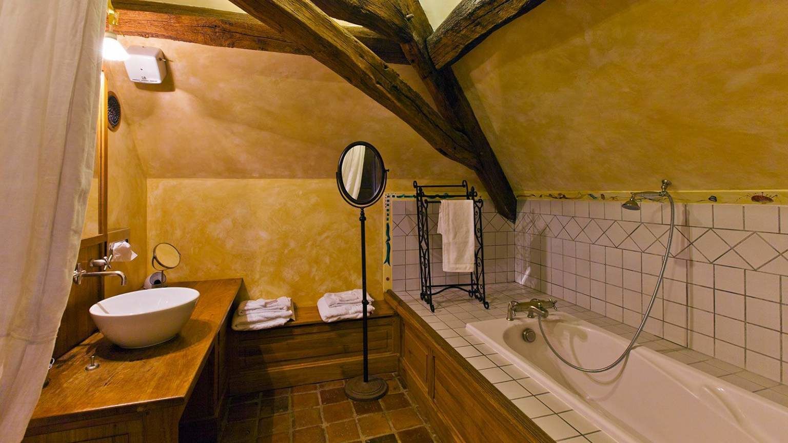 A bathroom with a wooden vanity, a large oval sink, a mirror, a bathtub with a showerhead, and a towel rack.