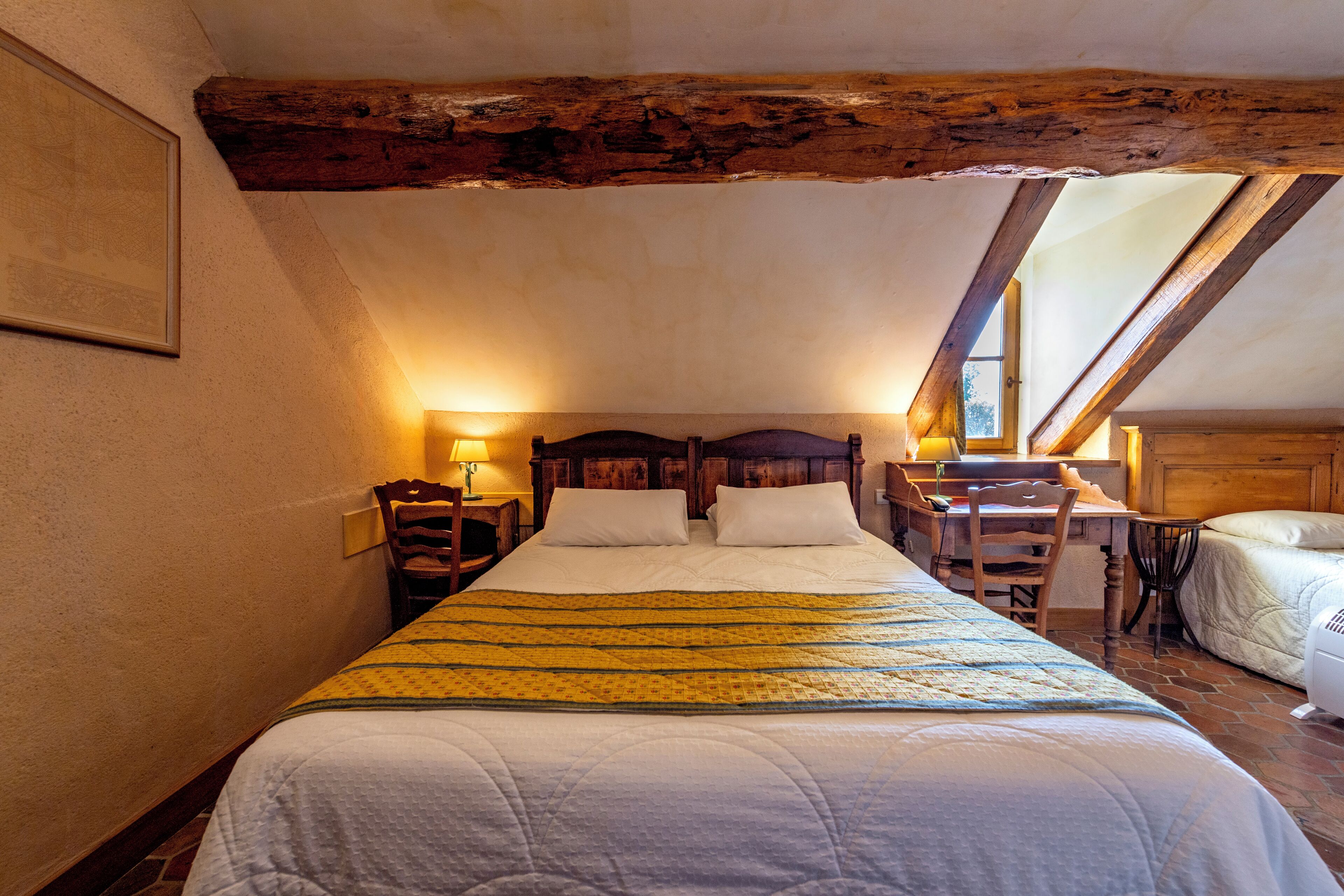 A bedroom with a wooden ceiling, a bed with white bedding, a wooden desk, and a chair.