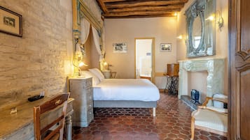 Un dormitorio con cama, cabecero de madera, mesita de noche, silla, cómoda, espejo y chimenea.