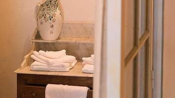 A bathroom with a marble countertop, a white pitcher with floral designs, and neatly folded towels on a wooden cabinet.