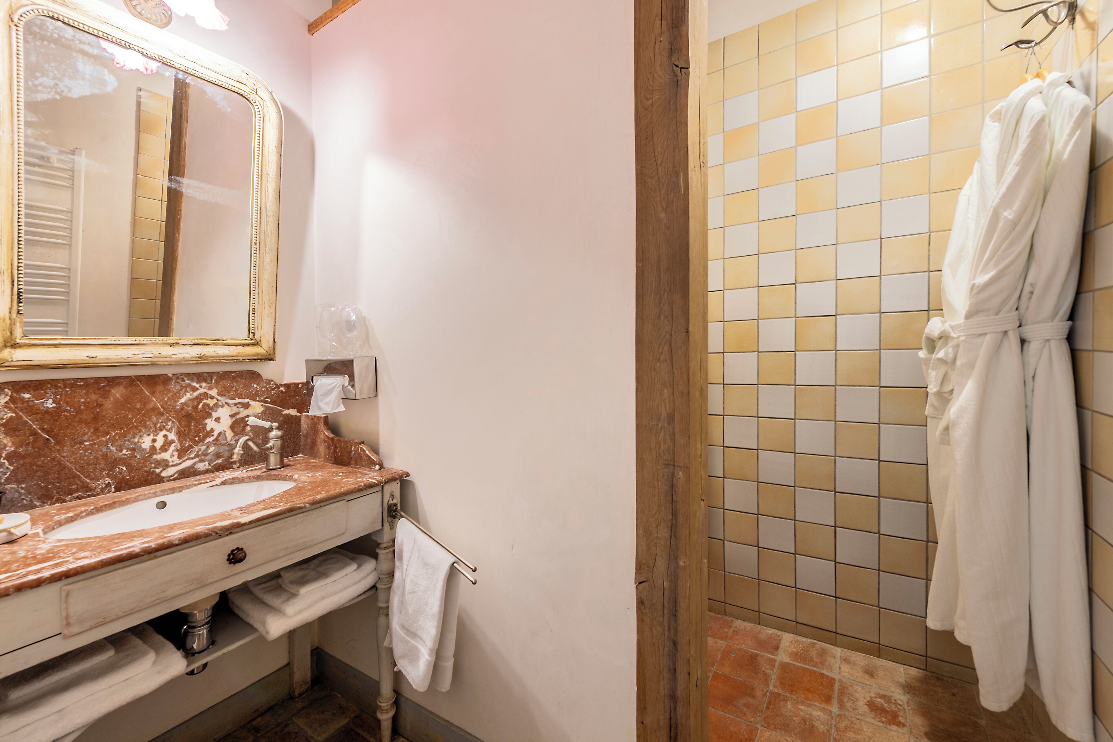 Casa de banho com lavatório de mármore, espelho, porta-toalhas e zona de duche revestida a azulejos.