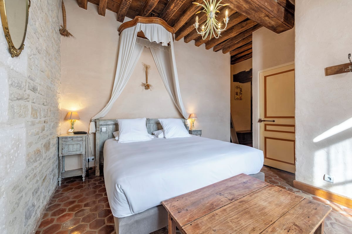 Un dormitorio con cama con dosel, cabecera de madera, paredes de piedra y una mesa de madera rústica.