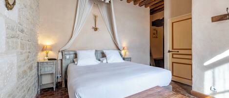 A bedroom with a four-poster bed, wooden headboard, stone walls, and a rustic wooden table.