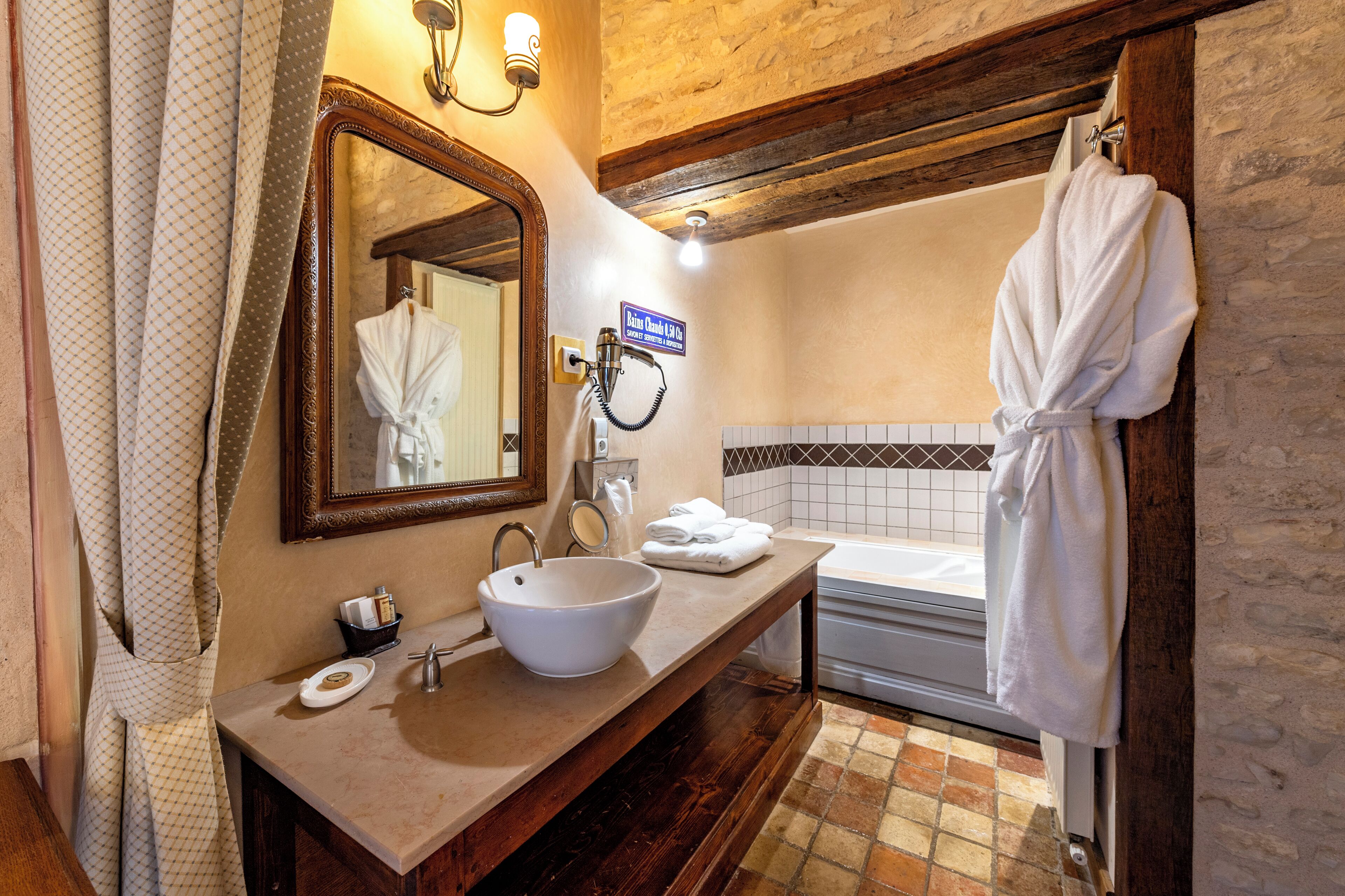 A bathroom with a large mirror, a sink, a bathtub, and a robe hanging on the wall.