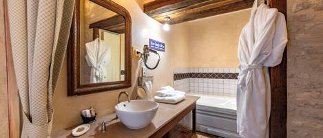 A bathroom with a large mirror, a sink, a bathtub, and a robe hanging on the wall.
