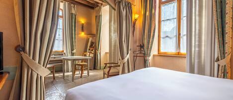 A hotel room with a large bed, a dining table with chairs, and curtains.