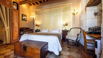 Una habitación tradicional con una cama grande, un cofre de madera, un escritorio con una máquina de escribir y un suelo de baldosas de piedra.