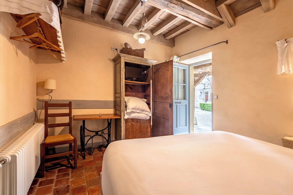 Un dormitorio con cama, una silla de madera, una mesa con lámpara, un radiador y un armario.