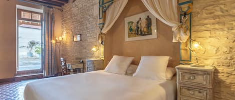 A bedroom with a large bed, stone walls, and a view through an open door.
