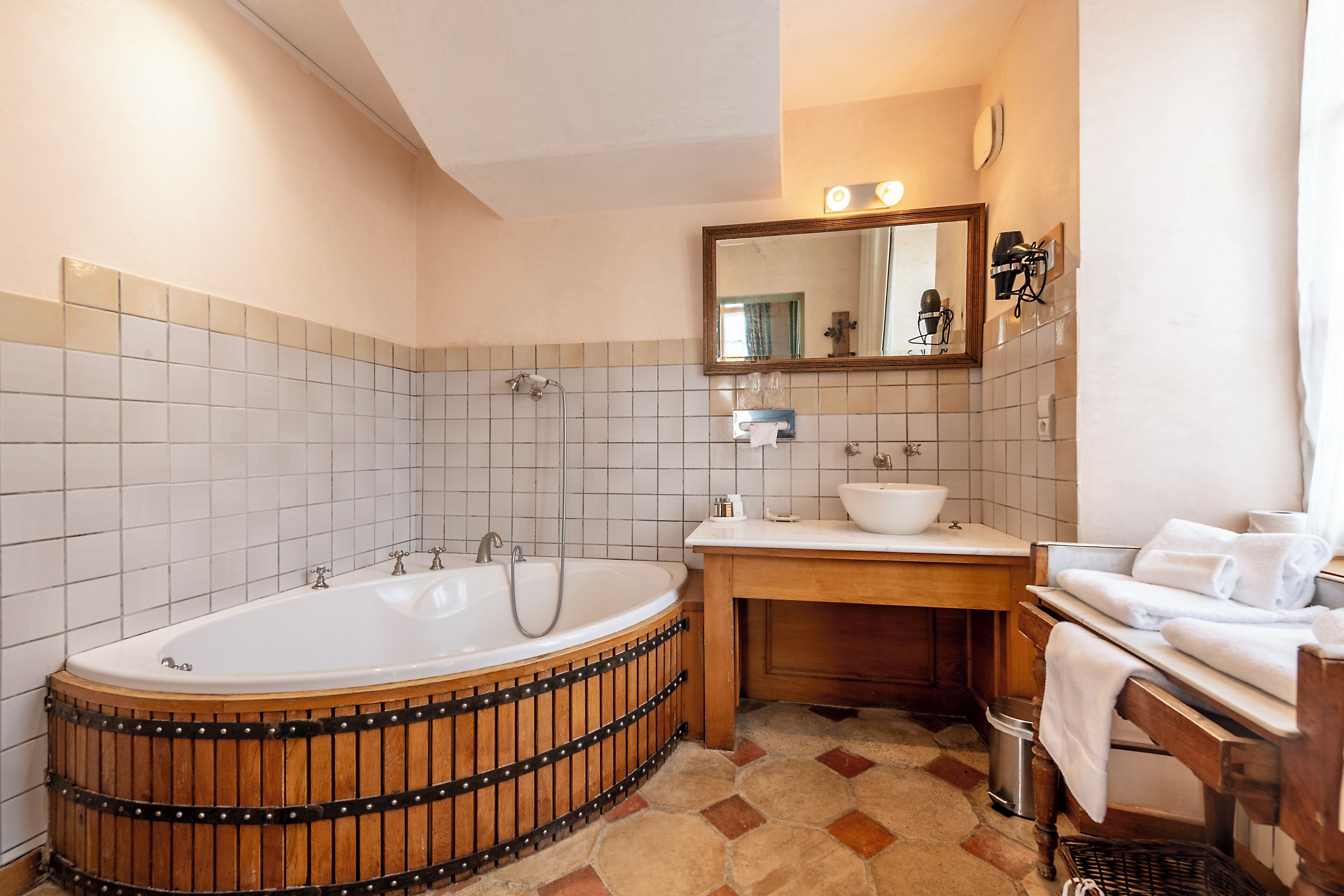 Un baño con bañera de madera, lavamanos, espejo y suelo de baldosas.