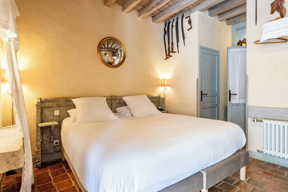 Un dormitorio con una cama grande, cabecera de madera, espejo redondo e iluminación montada en la pared.