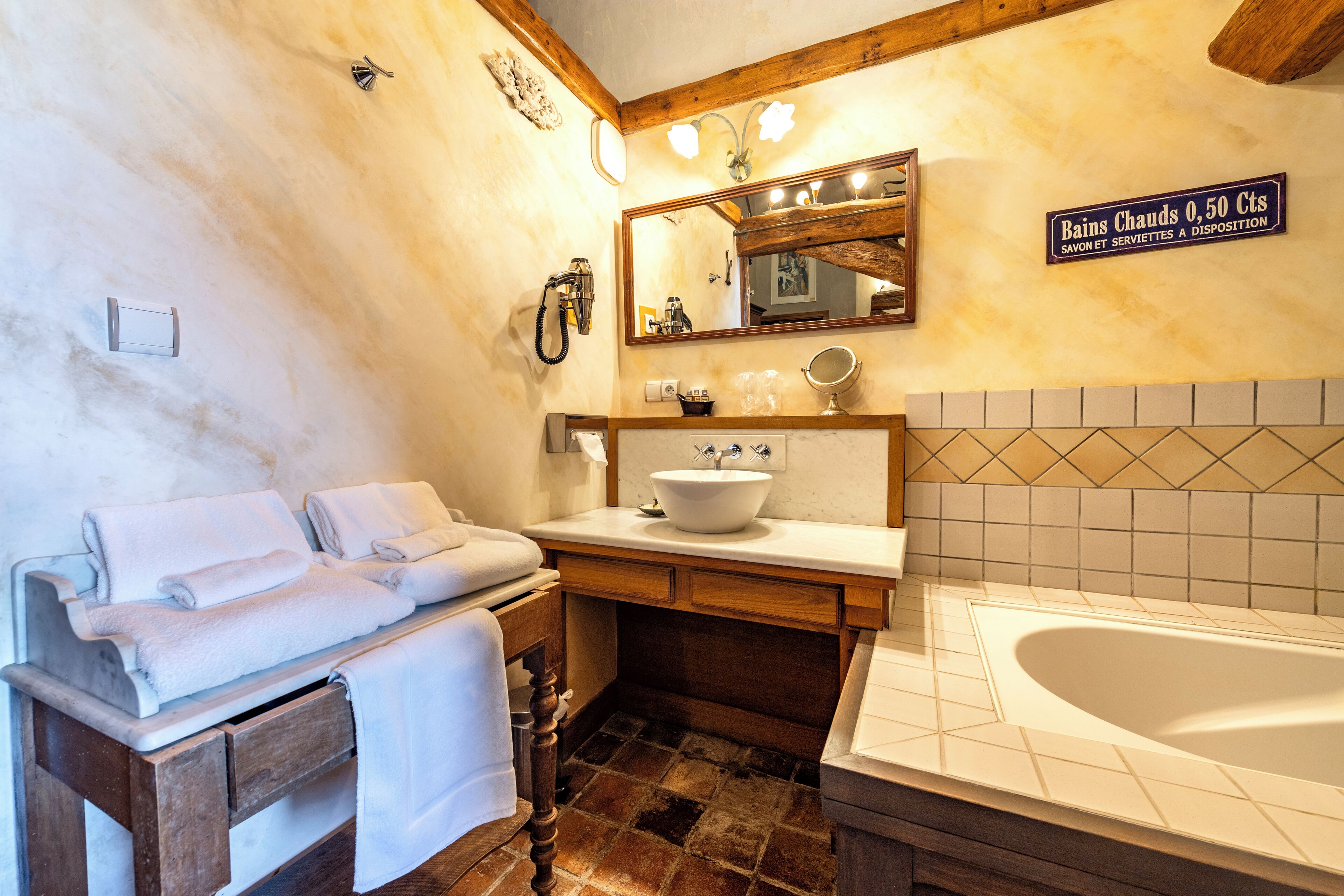 Un baño con bañera, lavabo y tocador con espejo. Hay un cartel en la pared que indica las comodidades del baño.
