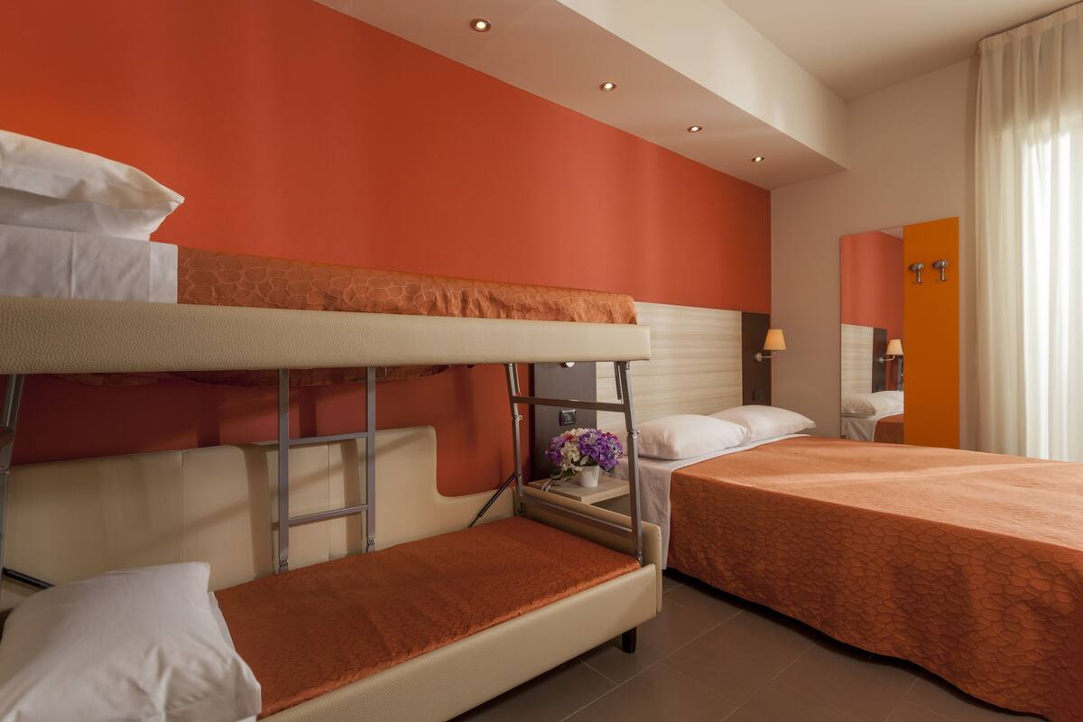 A hotel room with bunk beds, a bedside table with a lamp, and a mirror.
