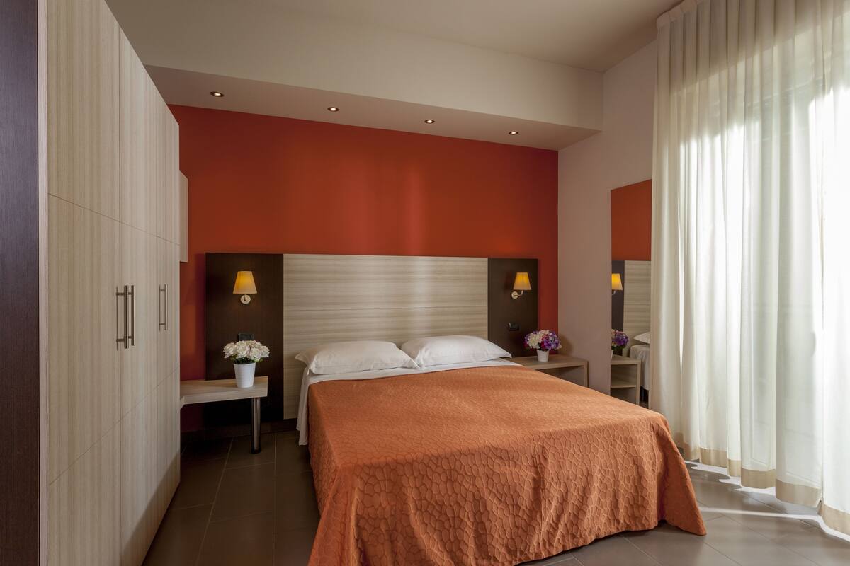 A modern bedroom with a large bed, two bedside lamps, and a nightstand with a vase of flowers.