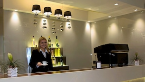 A hotel reception area with a counter, a piano, and a display of wine bottles. - Hotel Aurora Mare (Rimini)