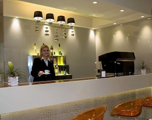 Zona de recepción de un hotel con mostrador, un piano y una exhibición de botellas de vino.
