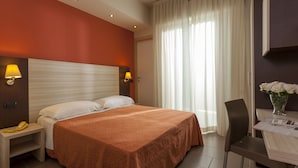 A hotel room with a large bed, two bedside lamps, a desk with a chair, and a window with curtains. - Hotel Aurora Mare (Rimini)