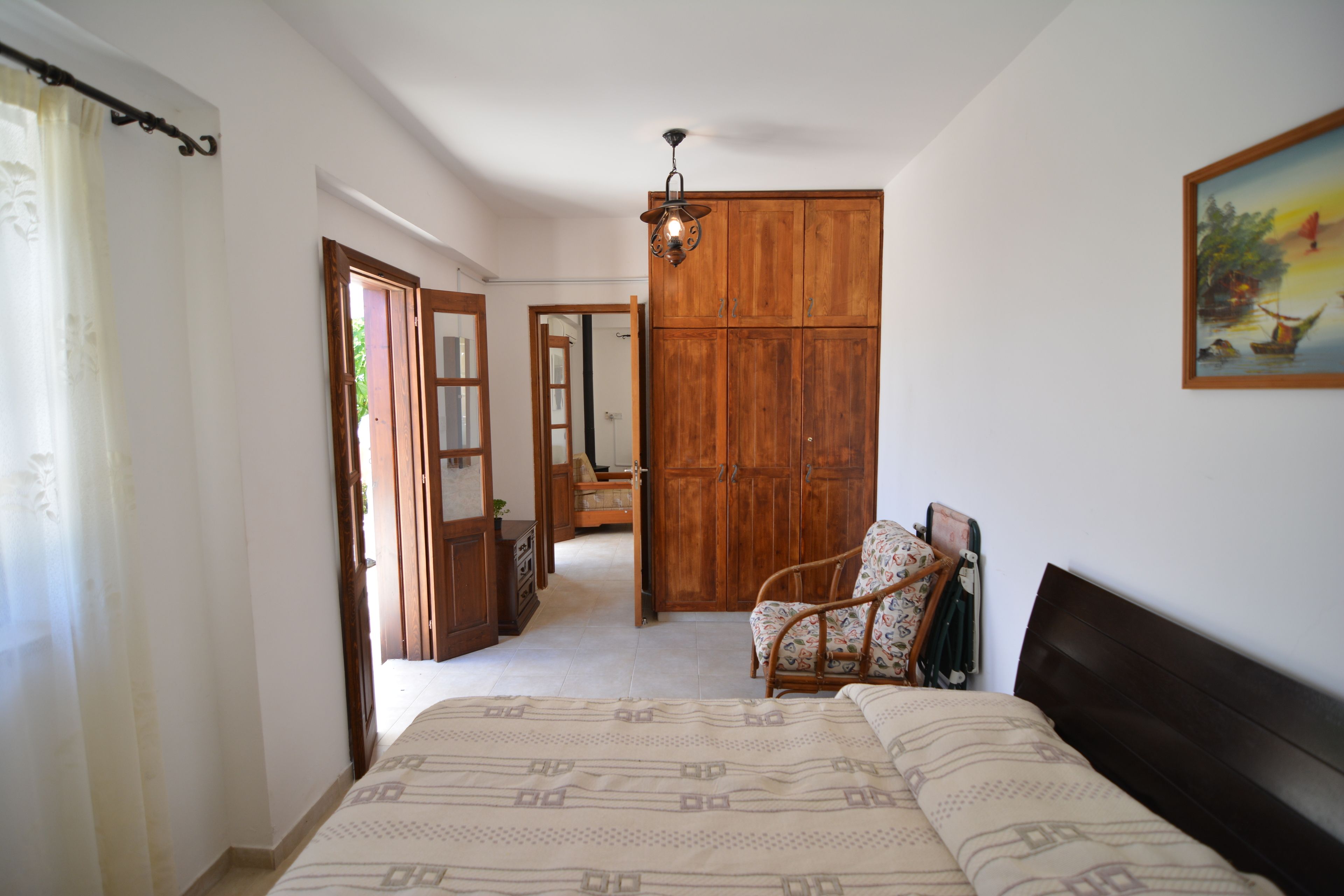 A bedroom with a bed, a wooden wardrobe, a chair, and a painting on the wall.
