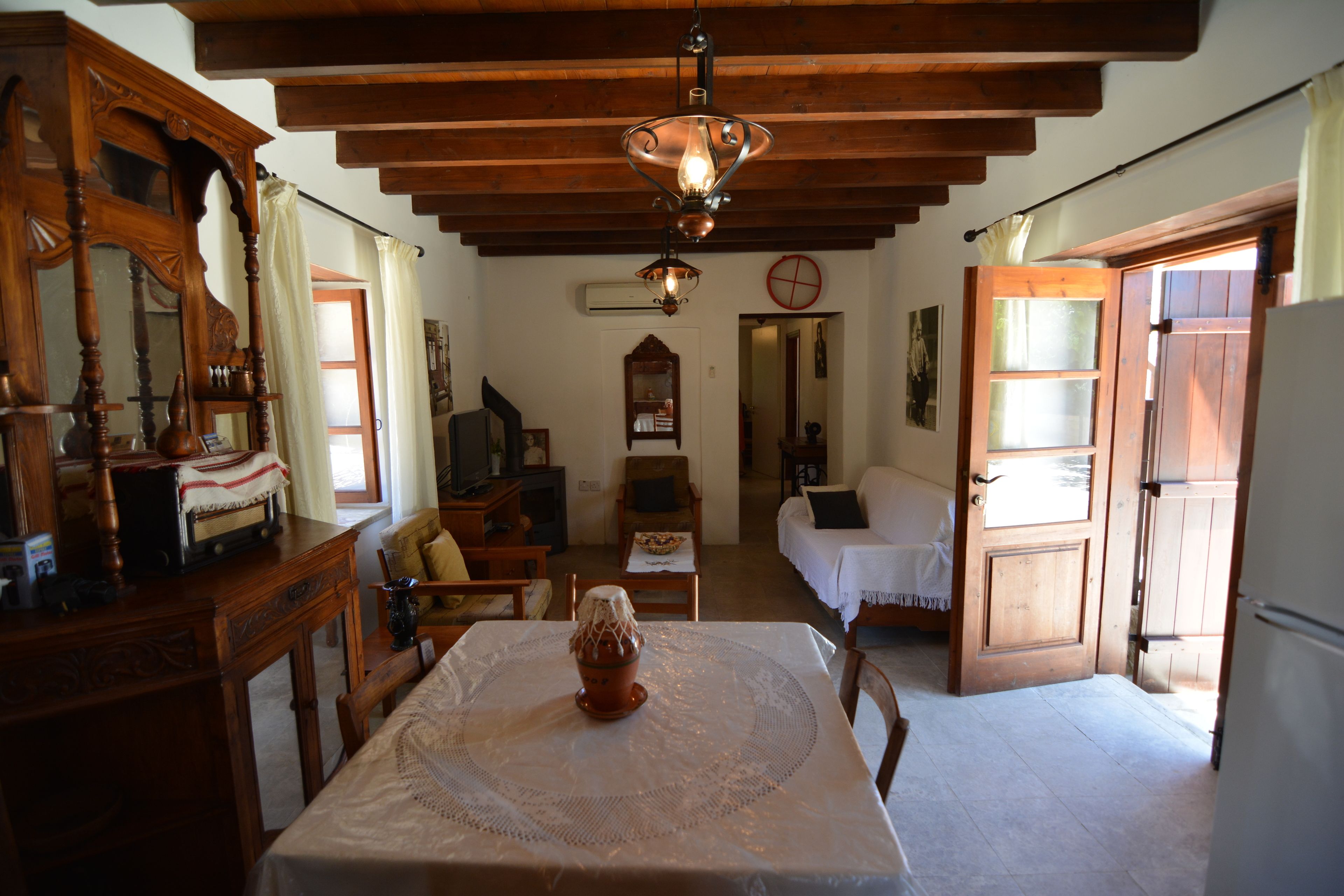 A cozy room with a wooden ceiling, a dining table with a lace tablecloth, a wooden cabinet, and a chair.