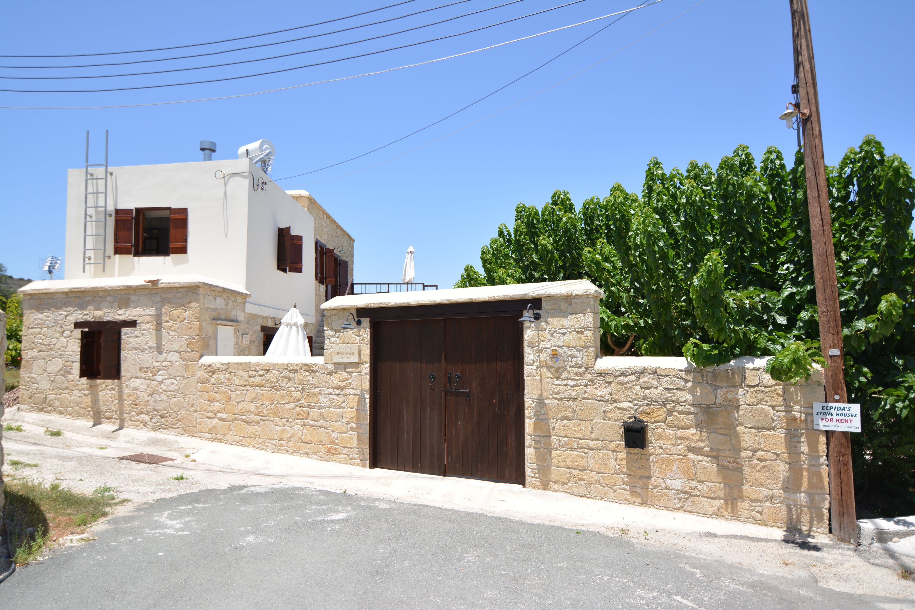 A stone house with a wooden door, a white umbrella, and a sign indicating it's for rent.