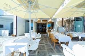 An outdoor dining area with white tables and chairs, covered by yellow umbrellas, and a stone floor. - San Michele (Procida)