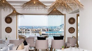 Ein Restaurant mit Tischen und Stühlen, Blick auf Boote und einen Yachthafen, und dekorative Wandteller.