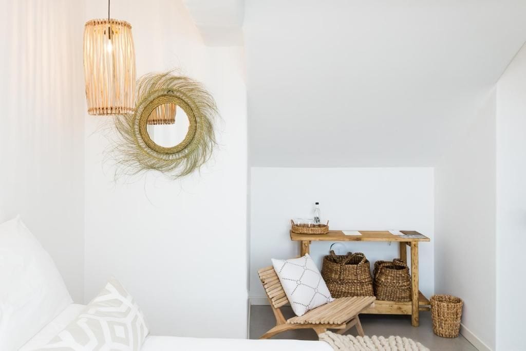 Habitación minimalista con un banco de madera, cestas de mimbre y una pequeña mesa de madera con una botella de agua.