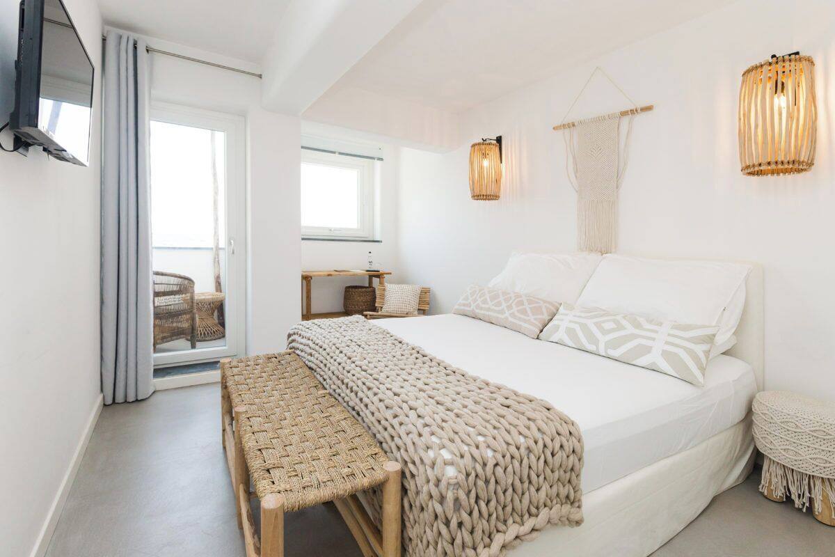 A bedroom with a large bed, a bench, a TV, and a view of the outside.