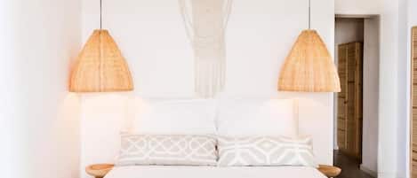 A bedroom with a bed, two hanging lamps, and a macrame wall hanging.