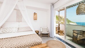 Ein Schlafzimmer mit Bett, einem Sessel und Meerblick durch ein großes Fenster.