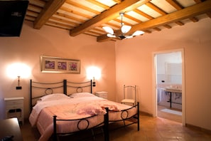 A bedroom with a bed, bedside tables, a chair, a ceiling fan, and a bathroom visible through an open door.