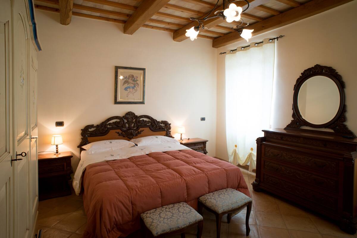 Ein Schlafzimmer mit einem hölzernen Bett, einem Nachttisch mit Lampe, einer Kommode mit Spiegel und einem gerahmten Bild an der Wand.