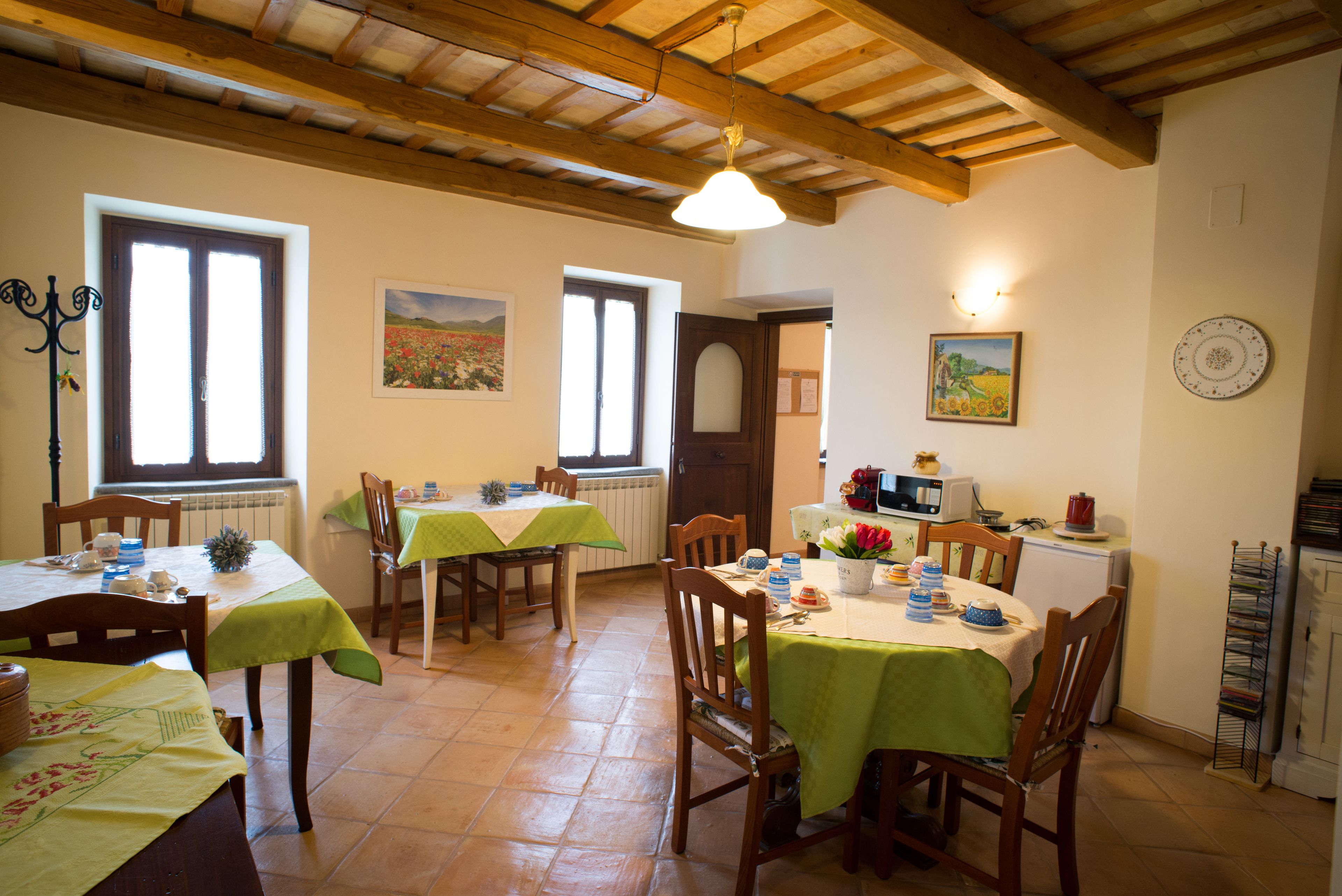 A dining area with wooden tables and chairs, a kitchen area with appliances, and a window with a view of a field.
