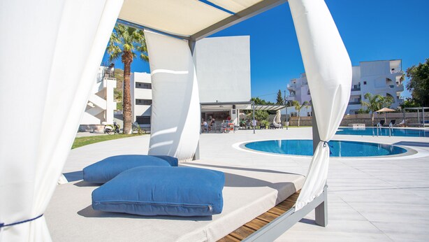 A poolside lounge area with a canopy, blue cushions, and a pool in the background. - Madison Boutique (Rhodes)