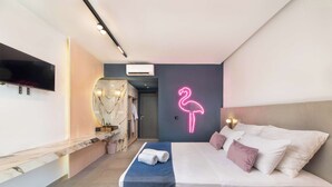 A modern hotel room with a bed, a TV, a neon flamingo sign, and a bathroom visible through an archway. - Madison Boutique (Rhodes)