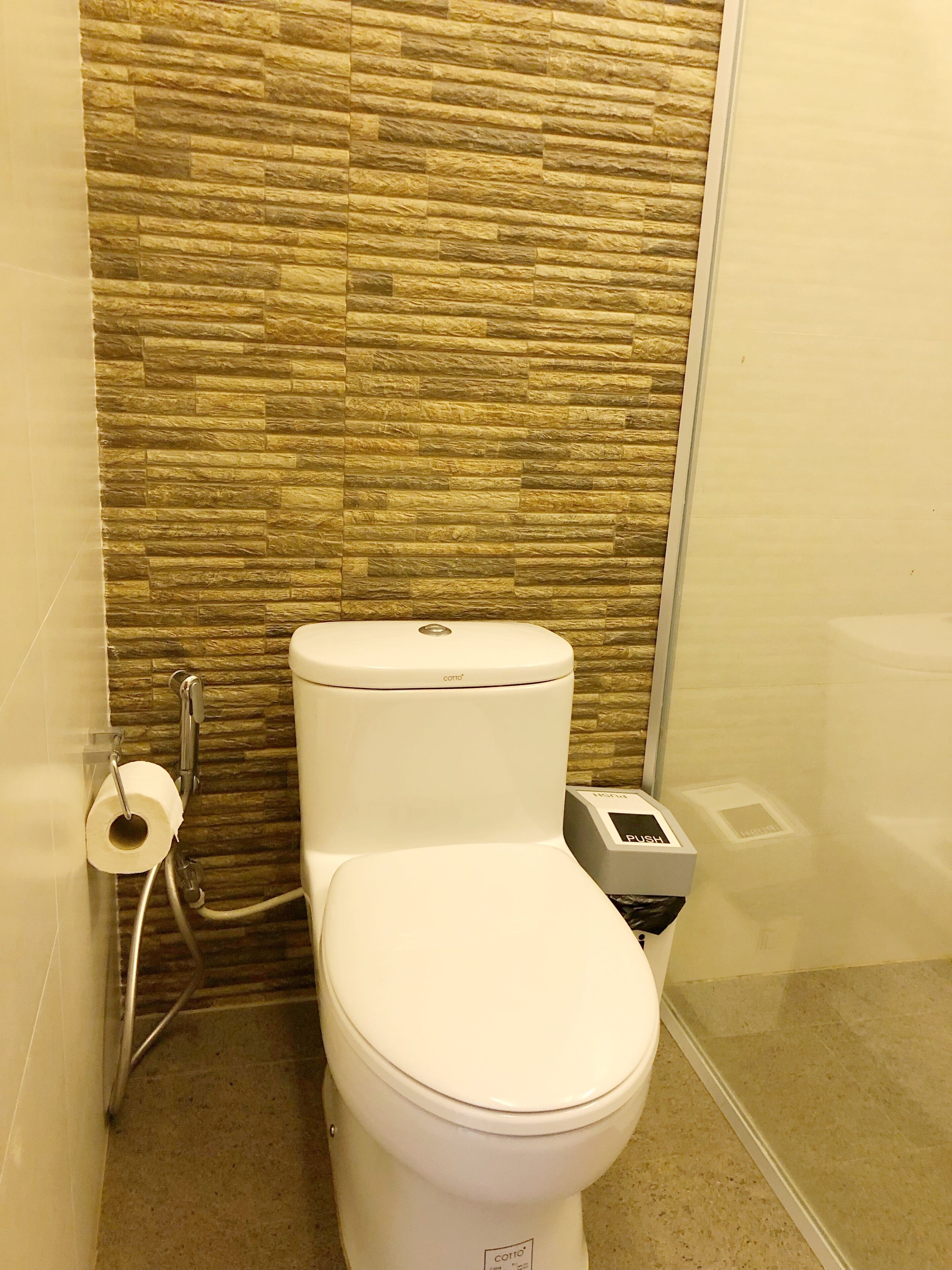 A toilet with a stone wall background, a toilet paper holder, and a bidet.