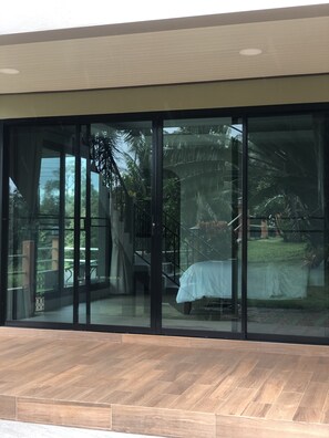 A modern building with large glass doors leading to a covered outdoor area with a wooden floor. - Sleep Soundly By The sea (Laem Ngop)