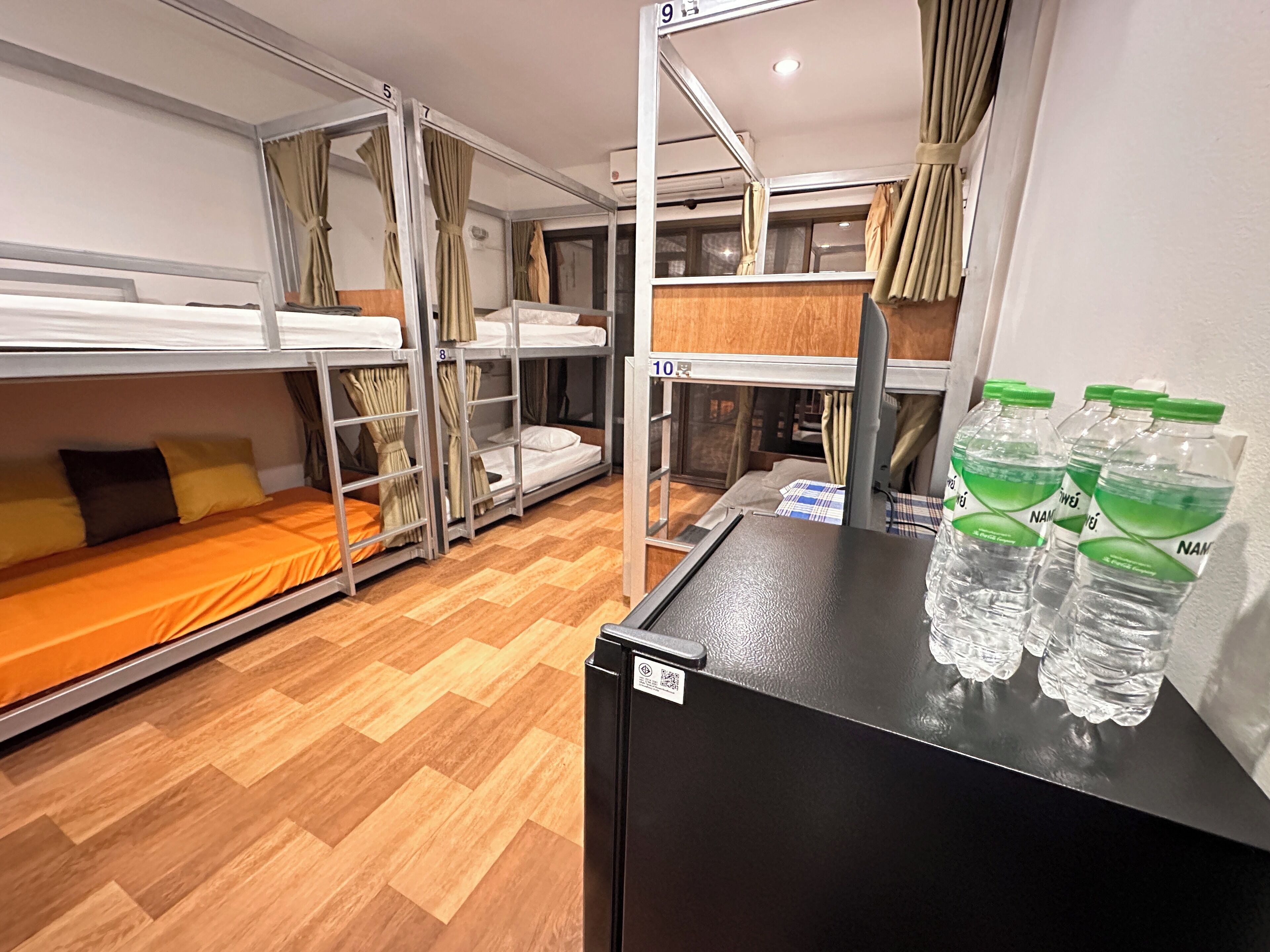 A dormitory room with bunk beds, a small table with water bottles, and a refrigerator.