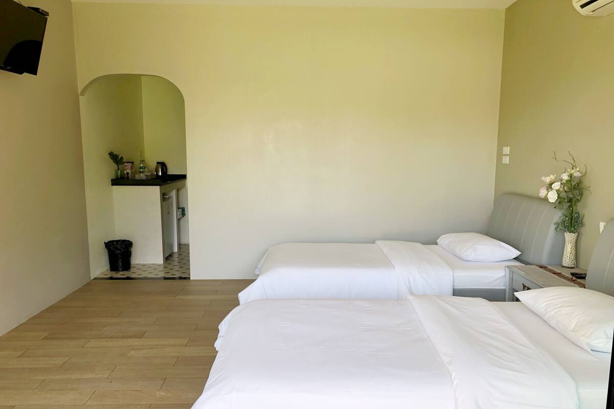Een hotelkamer met twee bedden, een kleine kitchenette en een houten vloer.