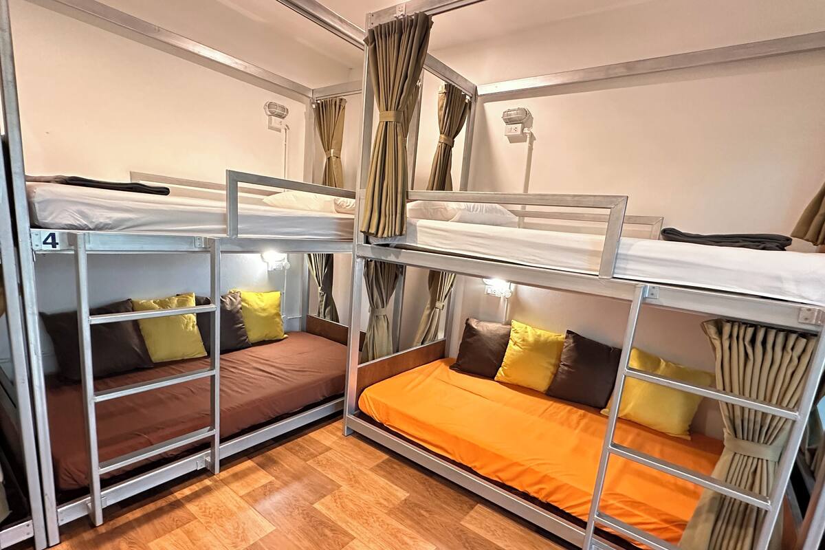 Een slaapkamer met stapelbedden, metalen frames, houten vloer en gordijnen.