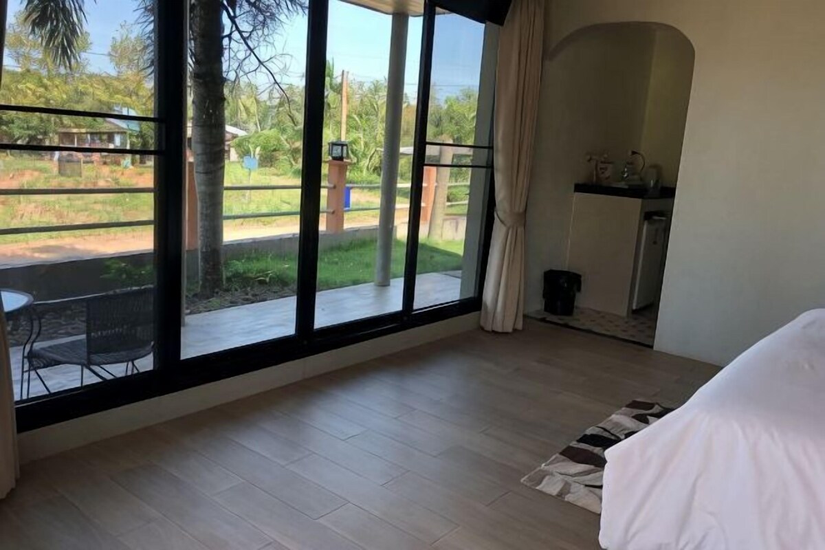 Quarto com uma janela grande, cama, mesinha e cadeira.