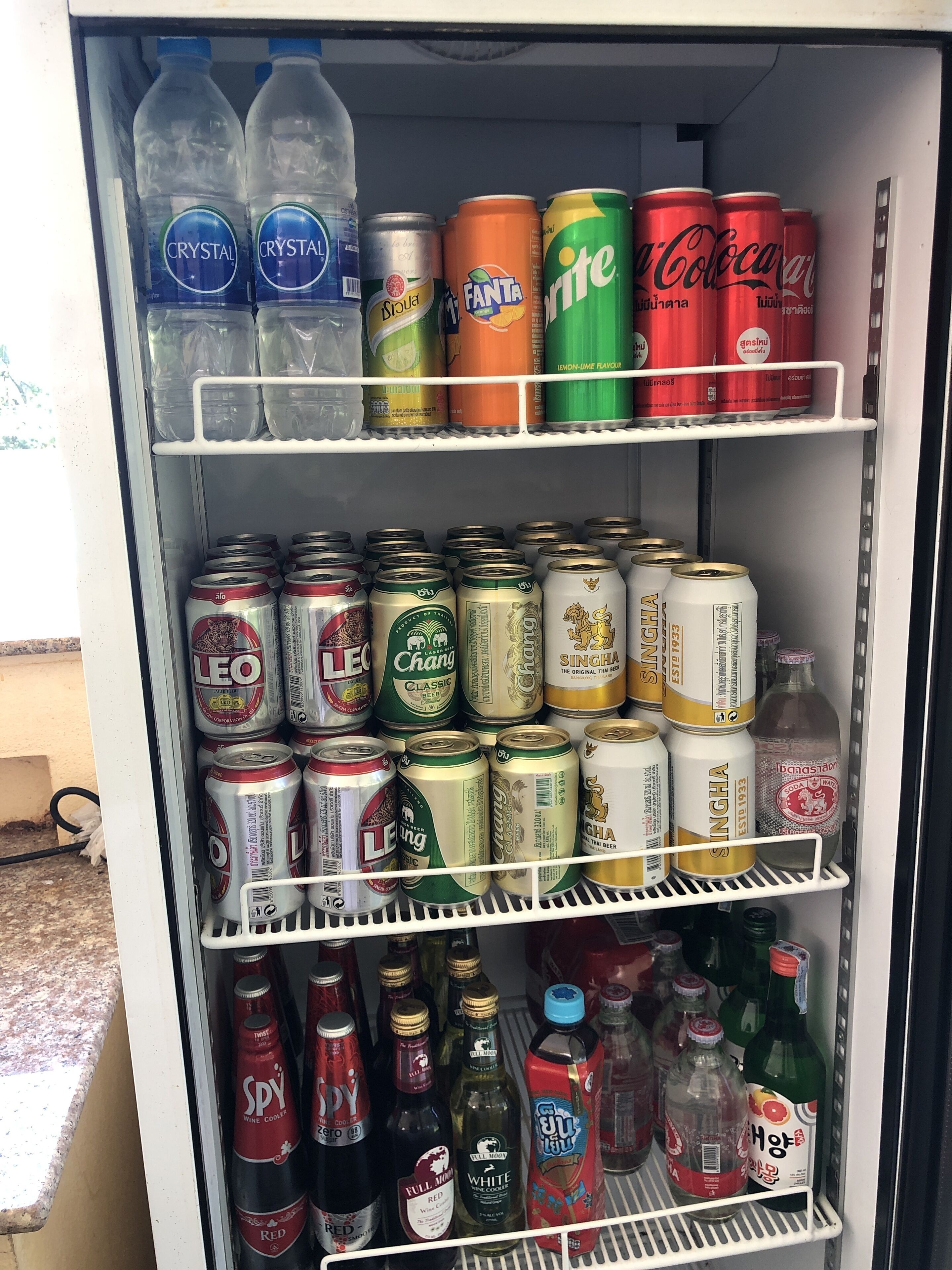 Ein Getränkekühlschrank, gefüllt mit verschiedenen Getränken, darunter Flaschenwasser, Dosen und alkoholische Getränke.