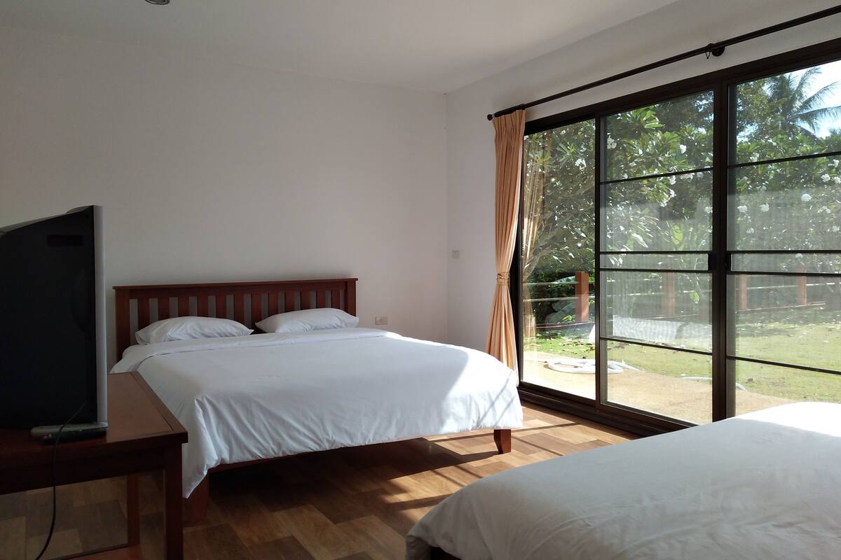 Een slaapkamer met een bed, een televisie op een tafel en een groot raam met gordijnen.