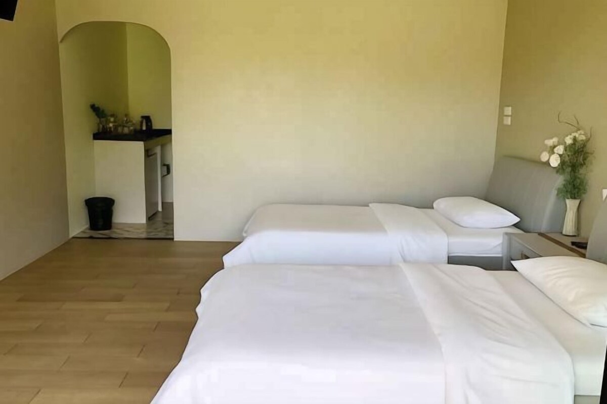 Quarto com duas camas, uma mesinha e uma planta.