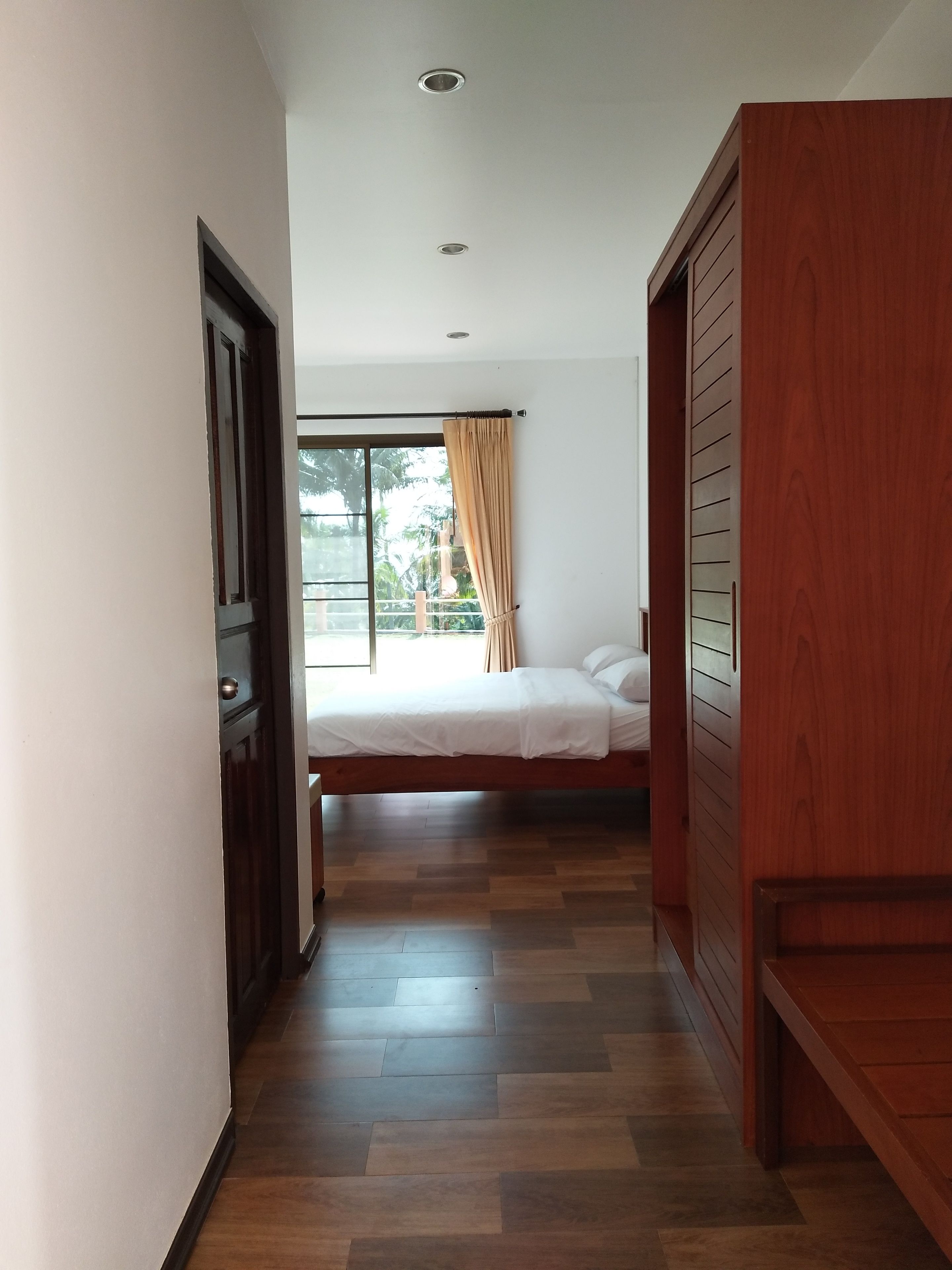 Un dormitorio con cama, ventana con cortinas y un armario de madera.