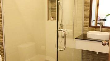 A modern bathroom with a glass-enclosed shower, a white toilet, and a sink with a mirror above it.