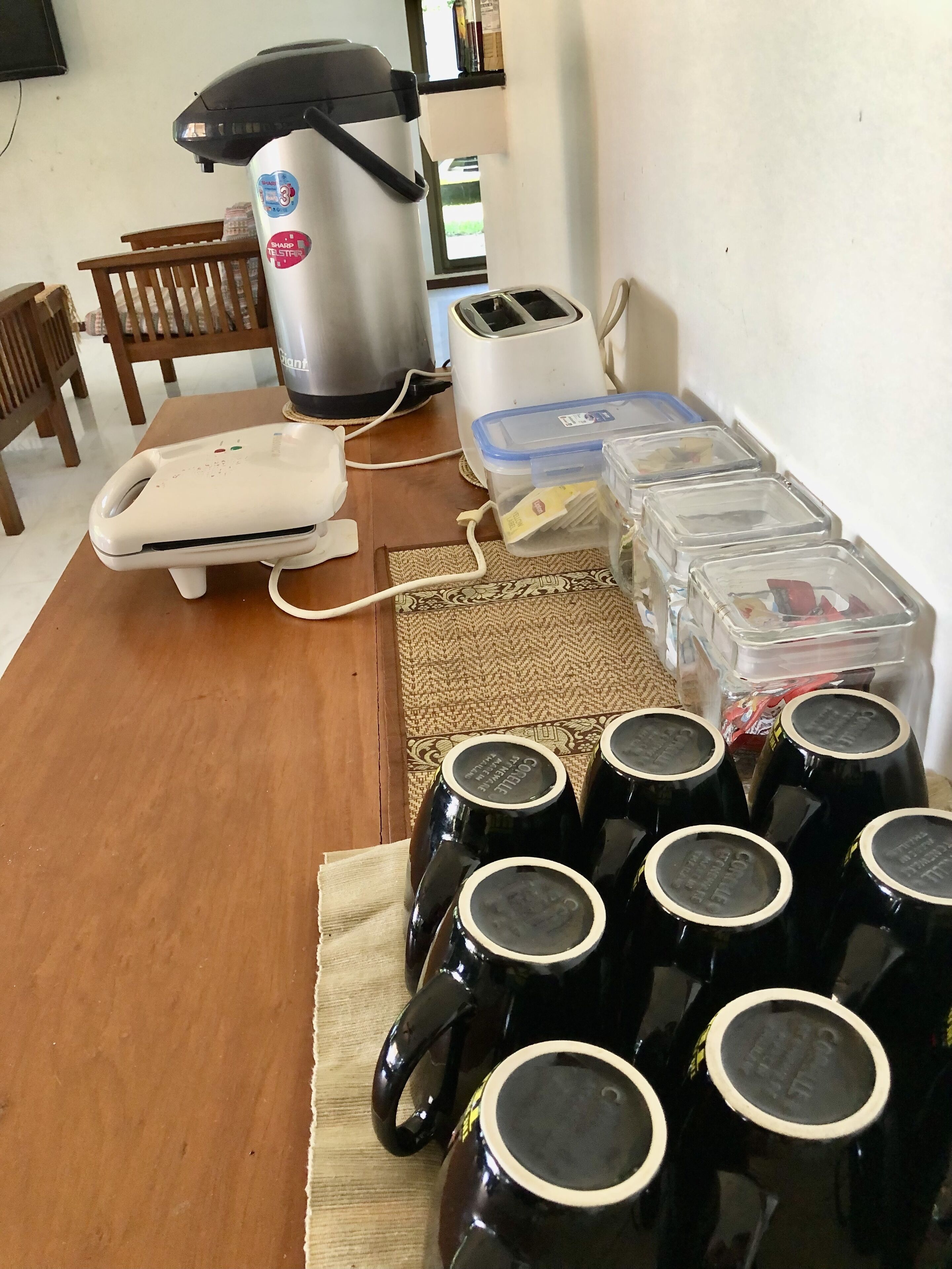 Een keukenhoek met een koffiezetapparaat, een broodrooster en plastic bakjes op een houten tafel.